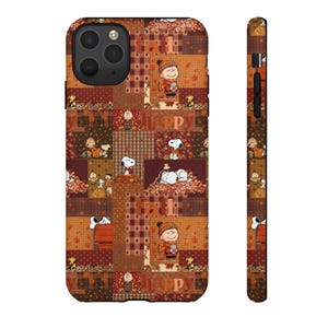 May include: A smartphone case featuring a patchwork design with Peanuts characters including Snoopy and Charlie Brown in autumn settings. The pattern includes brown, orange, and tan colors with falling leaves, plaid textures, and the text fall happy.