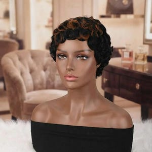 May include: A short, curly wig featuring a mix of black and warm brown tones. The hair is styled in tight, defined ringlets that frame the forehead and crown. The wig is displayed on a smooth, dark-toned mannequin head with neutral features.
