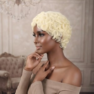 May include: A short, platinum blonde wig featuring tight, finger-wave curls that frame the head. The hair is styled in a cropped, pixie-length cut with a uniform, textured pattern of small, circular curls covering the entire scalp area.