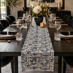 May include: A rectangular table runner featuring a dense, multi-layered graffiti print in black, white, and gold tones. The pattern consists of overlapping stylized tags, crowns, and abstract lettering covering the entire surface of the fabric.