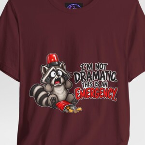 Puede incluir: Una camiseta color granate con el gráfico de un mapache que lleva una luz de emergencia roja en la cabeza y se sujeta la cara con gesto de sorpresa junto a una bolsa de patatas volcada. El texto dice I'M NOT DRAMATIC. THIS IS AN EMERGENCY en letras blancas y rojas.