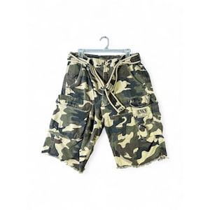 May include: Camouflage print cargo shorts featuring a green, brown, and tan pattern. The shorts include a matching fabric belt, multiple side cargo pockets, and a small rectangular patch on the left pocket with the text A|X Armani Exchange.