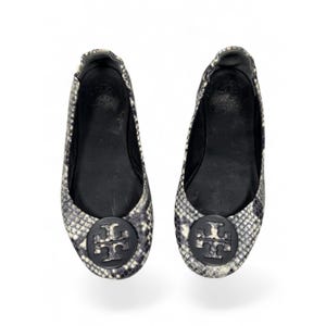 May include: A pair of slip-on ballet flats featuring a grey and white snakeskin pattern. Each shoe has a black circular emblem on the toe with a double T logo. The interior lining and footbed are black, and the edges are elasticized for a snug fit.