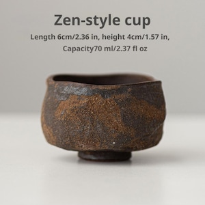 May include: A dark brown, textured cup with an irregular rim. Text above reads: Zen-style cup, Length 6cm/2.36 in, height 4cm/1.57 in, Capacity 70 ml/2.37 fl oz. The cup has a rough, mottled surface finish and a small circular base.