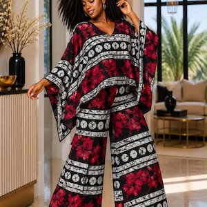 May include: A two-piece outfit consisting of a loose-fitting, V-neck poncho top with wide sleeves and matching wide-leg trousers. The fabric features a bold pattern of red floral motifs, black sections, and white bands with circular designs.
