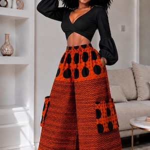 May include: A black long-sleeved crop top with a V-neckline and balloon sleeves paired with high-waisted wide-leg trousers. The trousers feature a vibrant orange and black pattern with large circular motifs and horizontal wavy lines, including side pockets.