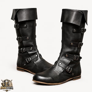 May include: A pair of black mid-calf boots featuring a wide fold-over cuff at the top. Each boot is secured with four horizontal straps across the front, each equipped with a metal buckle and silver-toned rivets. The boots have a flat sole.