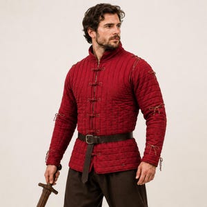 May include: A deep red quilted doublet featuring a high collar, vertical stitching, and front closures secured with thin cord ties. The long sleeves include matching cord ties at the shoulders and cuffs, paired with a dark brown leather belt.