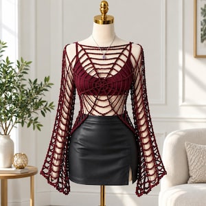 May include: A dark maroon crochet top featuring a spiderweb pattern with long, flared sleeves, worn over a matching maroon tank top. The garment is displayed on a mannequin alongside a black leather-look mini skirt with a side slit detail.