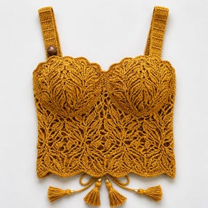 Può includere: Un top corto all'uncinetto color giallo senape caratterizzato da un design a bustier strutturato con intricati motivi a foglia su tutto il corpo. Il capo presenta spalline larghe, un orlo smerlato e quattro nappe pendenti sul bordo.