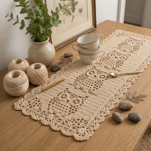 May include: A rectangular beige crochet table runner featuring a repeating owl pattern and a scalloped lace border. The runner is crafted from light-colored yarn and displays intricate openwork details throughout the design of the owls.