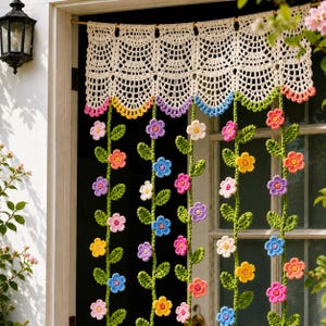 May include: A cream-coloured crocheted valance featuring a scalloped edge with pink, yellow, purple, and blue accents. Hanging from the valance are multiple vertical green crocheted vines adorned with small, multi-coloured flowers in various shades.