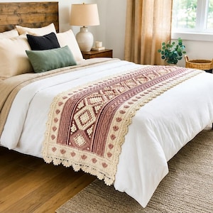 May include: A rectangular crochet bed runner featuring a central diamond pattern in cream and dusty rose, accented with bobble stitches and cable textures. The edges are finished with a scalloped cream border and small floral motifs.