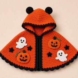 Può includere: Una mantella con cappuccio all'uncinetto di colore arancione con bordo smerlato nero e due piccole orecchie nere sulla parte superiore. La mantella è decorata con due applicazioni di fantasmi bianchi, due zucche arancioni con piccioli verdi e diverse piccole stelle nere.
