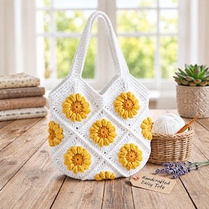May include: A white crochet tote bag featuring a repeating diamond pattern with raised, textured yellow and orange sunflower motifs. The bag has two integrated handles and a small rectangular tag attached that reads Handcrafted Daisy Tote.