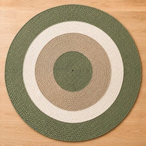Può includere: Un tappeto circolare con un motivo concentrico di anelli all'uncinetto in colori alternati. Il design è composto da un centro verde oliva scuro, seguito da una fascia color marrone chiaro, un anello più ampio color crema e un bordo verde oliva.