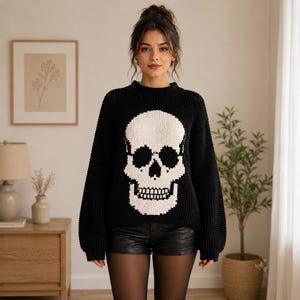 Peut inclure: Un pull en tricot noir à manches longues avec un grand motif de crâne blanc centré sur le devant. Le pull présente un col rond côtelé, des poignets côtelés et un ourlet côtelé, réalisé avec un motif en tricot épais et texturé.