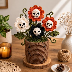 Può includere: Una pianta in uncinetto in vaso con quattro fiori dotati di centri a forma di teschio bianchi, arancioni e neri. I fiori hanno steli e foglie verdi e sono piantati in un vaso in uncinetto marrone testurizzato con piccoli dettagli cuciti.