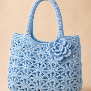 Può includere: Una borsa tote all'uncinetto color azzurro con un intricato motivo a ventaglio traforato su tutto il corpo. La borsa include due robusti manici abbinati e un decoro floreale tridimensionale all'uncinetto fissato sul lato superiore destro.