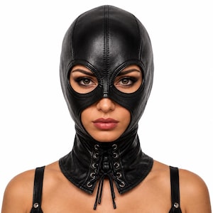 Puede incluir: Una capucha de aspecto de cuero negro con un diseño de cara completa y aberturas circulares para los ojos. La capucha incluye una costura vertical que recorre el centro y una sección frontal en el cuello asegurada con ojales metálicos y cordones negros.