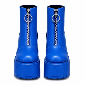 May include: A pair of bright blue ankle boots featuring a thick platform sole with a treaded base. Each boot has a front-facing silver zipper closure that extends from the top of the shaft to the toe, finished with a circular silver ring pull.