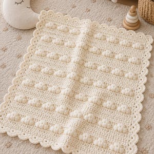 May include: A rectangular cream-colored crochet blanket featuring a repeating pattern of raised bobble-stitch clouds arranged in horizontal rows. The blanket is finished with a decorative scalloped edge border, creating a textured surface design.