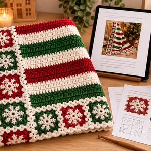 Puede incluir: Una manta de ganchillo con un borde de cuadrados alternos rojos y verdes con motivos de copos de nieve blancos, y una sección central de rayas horizontales en rojo, verde y crema. La manta se muestra junto a una tableta y un patrón.