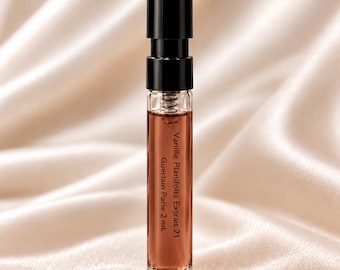 Op de afbeelding: Een klein parfummonsterflesje van helder glas met een zwarte dop, gevuld met een amberkleurige vloeistof. Het etiket op de voorzijde vermeldt Vanille Planifolia Extrait 21, Guerlain Paris 2 ml. Het flesje heeft een cilindrische en eenvoudige vorm.