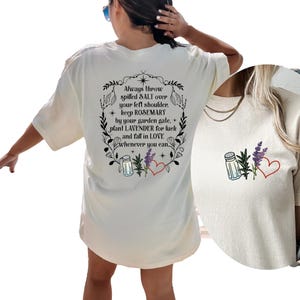 May include: An off-white t-shirt featuring a black graphic on the back with the text: Always throw spilled SALT over your left shoulder, keep ROSEMARY by your garden gate, plant LAVENDER for luck and fall in LOVE whenever you can, with icons.
