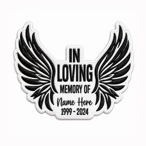 Könnte beinhalten: Ein weißer, bestickter Aufnäher mit schwarzen Engelsflügeln auf beiden Seiten. Der mittlere Text lautet IN LOVING MEMORY OF, gefolgt von dem Platzhalter Name Here und den Jahren 1999-2024 in einer fetten, schwarzen Schriftart.