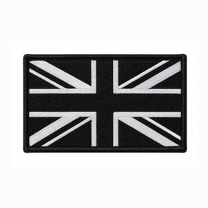 Puede incluir: Un parche rectangular bordado que presenta el diseño de la bandera Union Jack en un esquema de color monocromático blanco y negro. El diseño consiste en una cruz central y franjas diagonales en hilo blanco sobre un fondo negro sólido.
