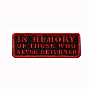 May include: A rectangular embroidered patch with a black background and a red border. The text IN MEMORY OF THOSE WHO NEVER RETURNED is stitched in red capital letters across the centre of the patch, featuring a bold and clear font style.