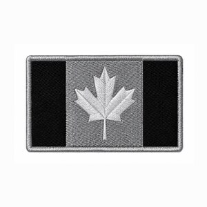 Puede incluir: Un parche rectangular bordado con un diseño estilizado de la bandera canadiense. El parche tiene dos paneles laterales verticales de color negro sólido y un panel central gris que contiene una hoja de arce blanca bordada. Borde gris cosido.
