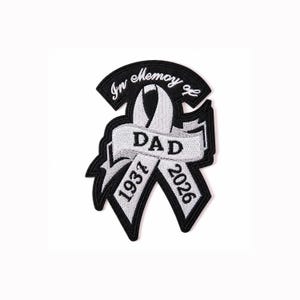 May include: A black and white embroidered patch featuring a ribbon design. The text reads In Memoy of DAD with the years 1937 and 2026 stitched into the ribbon. The patch has a black border and white lettering, designed for attachment to fabric items.