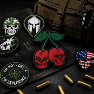 May include: A collection of tactical morale patches including a cherry skull design, a Spartan helmet, a skull in a camouflage helmet, a compass patch with the text I'M NOT LOST I'M EXPLORING, and a skull with an American flag pattern.