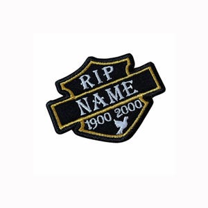 Może przedstawiać: Czarna haftowana naszywka w kształcie tarczy ze złotą obwódką. Napis RIP NAME jest wyhaftowany na biało, a poniżej znajdują się cyfry 1900 2000 oraz mała ikona białej gołębicy. Wzór zawiera element w formie poziomego baneru.