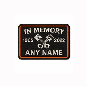 Könnte beinhalten: Ein rechteckiger bestickter Aufnäher mit schwarzem Hintergrund und orangefarbenem Rand. Er zeigt den weißen Text IN MEMORY, 1965, 2022 und ANY NAME sowie eine zentrale Grafik aus zwei gekreuzten Motorkolben in weißem Garn.