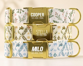 May include: Three pet collars with gold-tone metal buckles and hardware. Each buckle is engraved with a name and phone number: COOPER 123-456-7890, STELLA 123-456-7890, and MILO 123-456-7890. The fabric straps feature white backgrounds with patterns of green pine branches, red berries, and gold snowflakes.
