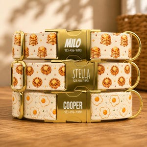 May include: Three pet collars with gold-tone metal buckles. The top collar features a pancake pattern with the name MILO and 123-456-7890. The middle collar has a waffle pattern with the name STELLA and 123-456-7890. The bottom collar has an egg pattern with the name COOPER and 123-456-7890.