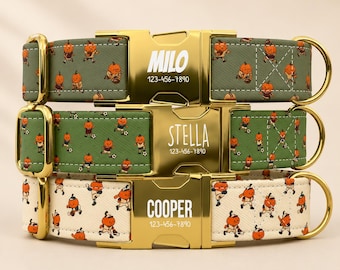 May include: Three pet collars with gold-tone metal buckles engraved with names and phone numbers. Two collars are olive green with a pumpkin character pattern, and one is cream with a pumpkin baseball player pattern, all featuring gold D-rings.