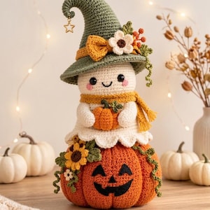 May include: A crocheted ghost figurine wearing a green pointed hat with a gold star charm, a yellow scarf, and holding a small orange pumpkin. The ghost sits atop a large orange jack-o'-lantern decorated with crocheted sunflowers and green vines.
