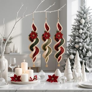 Könnte beinhalten: Drei hängende Spiralornamente aus gehäkeltem Garn in den Farben Dunkelrot, Waldgrün und Creme. Jedes Ornament ist oben mit einer auffälligen roten Weihnachtssternblüte und unten mit einem kleinen goldenen Sternanhänger versehen.