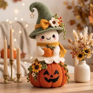 May include: A crocheted ghost figure wearing a green pointed hat with a star charm, a yellow scarf, and holding a small orange pumpkin. The ghost sits atop a large, round, orange crocheted pumpkin with a black stitched jack-o'-lantern face.