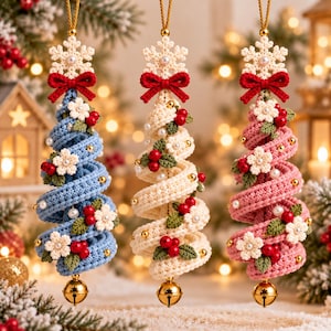 Puede incluir: Tres adornos navideños en espiral hechos de hilo de ganchillo en azul, crema y rosa. Cada uno presenta un copo de nieve blanco, un lazo rojo, flores blancas, hojas verdes, bayas rojas, cuentas doradas y un cascabel dorado.