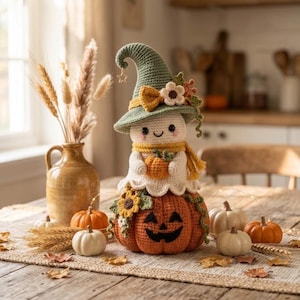 May include: A crocheted ghost figure wearing a sage green pointed hat with a small star charm, a yellow scarf, and holding a tiny orange pumpkin. The ghost sits atop a large, round, orange crocheted pumpkin with a black stitched jack-o'-lantern face.