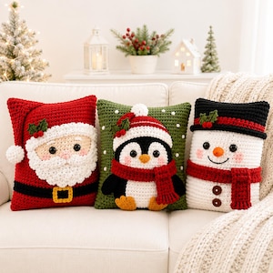 May include: Three square crochet pillows featuring holiday characters. The left pillow is a red Santa Claus with a white beard and black belt. The center pillow is green with a penguin wearing a red scarf. The right pillow is a white snowman.