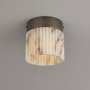 May include: A cylindrical flush mount ceiling light fixture featuring a dark bronze metal base and a fluted, translucent white alabaster shade with natural grey veining patterns throughout the stone surface, creating a warm, diffused light effect.