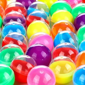 May include: A collection of numerous spherical plastic capsules in a variety of vibrant colors including red, blue, yellow, green, orange, and purple. Each capsule is constructed from two interlocking halves, with one side being clear and the other side opaque.
