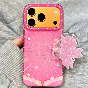 May include: A pink smartphone case featuring a central embossed cupid graphic with a bow and arrow, surrounded by radiating lines and small stars. A matching translucent cupid-shaped phone grip is attached to the right side. The text OHGODesign is visible.