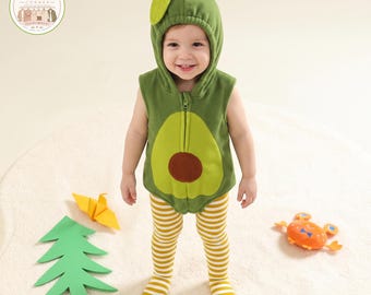 Op de afbeelding: Een mouwloos groen vest met capuchon in avocado-thema met een rits aan de voorzijde, voorzien van een lichtgroen middenpaneel en een bruine ronde patch. De outfit bevat een wit en geel horizontaal gestreepte maillot met voetjes.